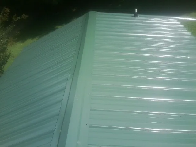 New green metal panels meeting at the ridge of a roof — Flat Roof Repair work by our crew in Russell