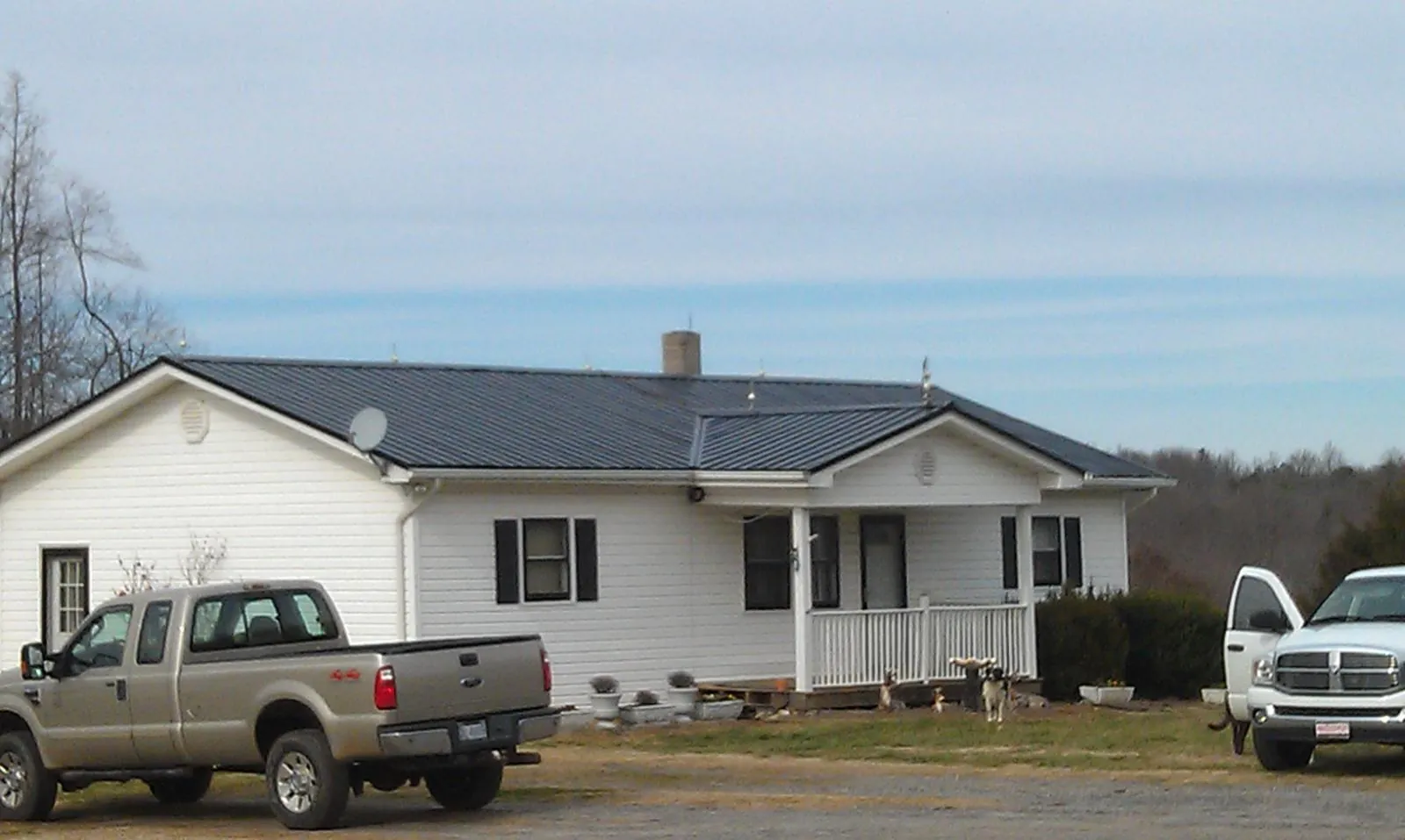 Finished dark metal roof on a white ranch home with work trucks parked in Russell